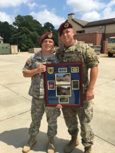 Two Caucasian men are standing in military uniform with red berets behind a board covered in papers celebrating them.